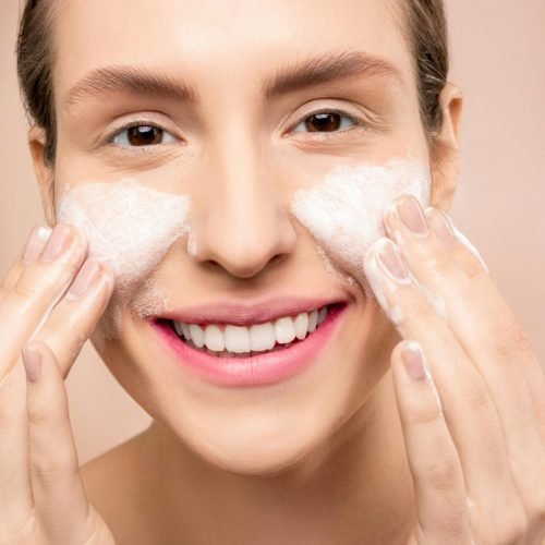 Close-up of a woman happily washing her face with foamy cleanser.
